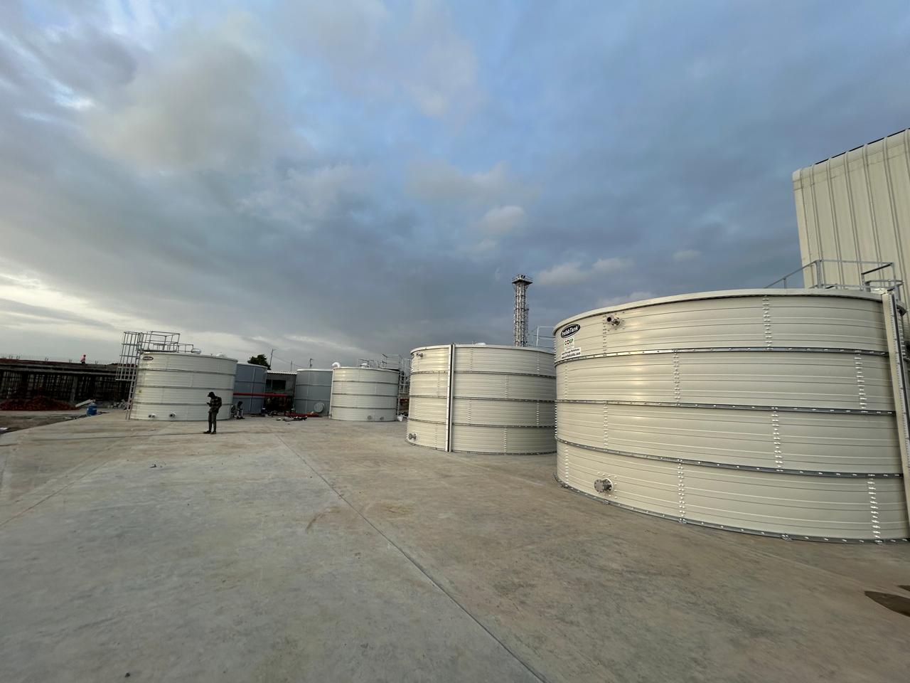 Multiple white Zinc Aluminium Steel tanks on a concrete yard under dramatic clouds
